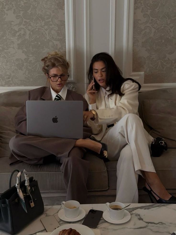 Two women sitting on a couch with a laptop, engaged in a conversation.