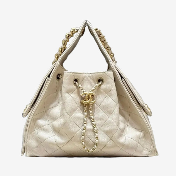 Beige quilted handbag with gold chain detail on a white box with Chanel branding in the background.