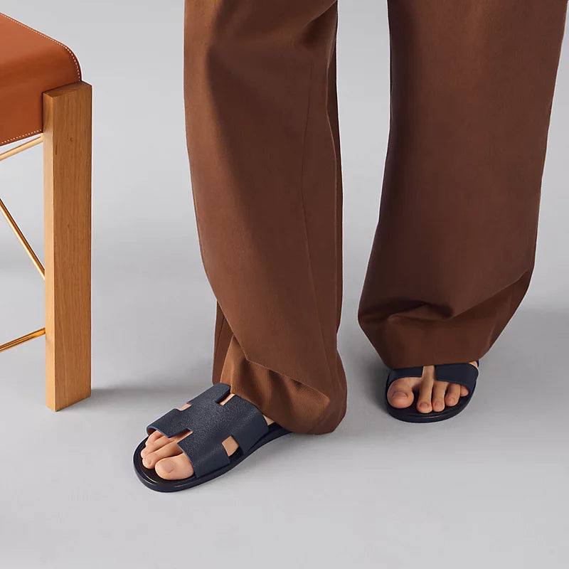 Person wearing brown pants and navy sandals on a light gray background